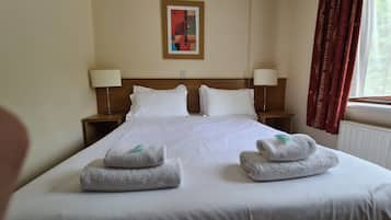 Quarto de hotel com uma cama grande, duas mesas de cabeceira com luminárias, um quadro na parede e uma janela com cortinas.
