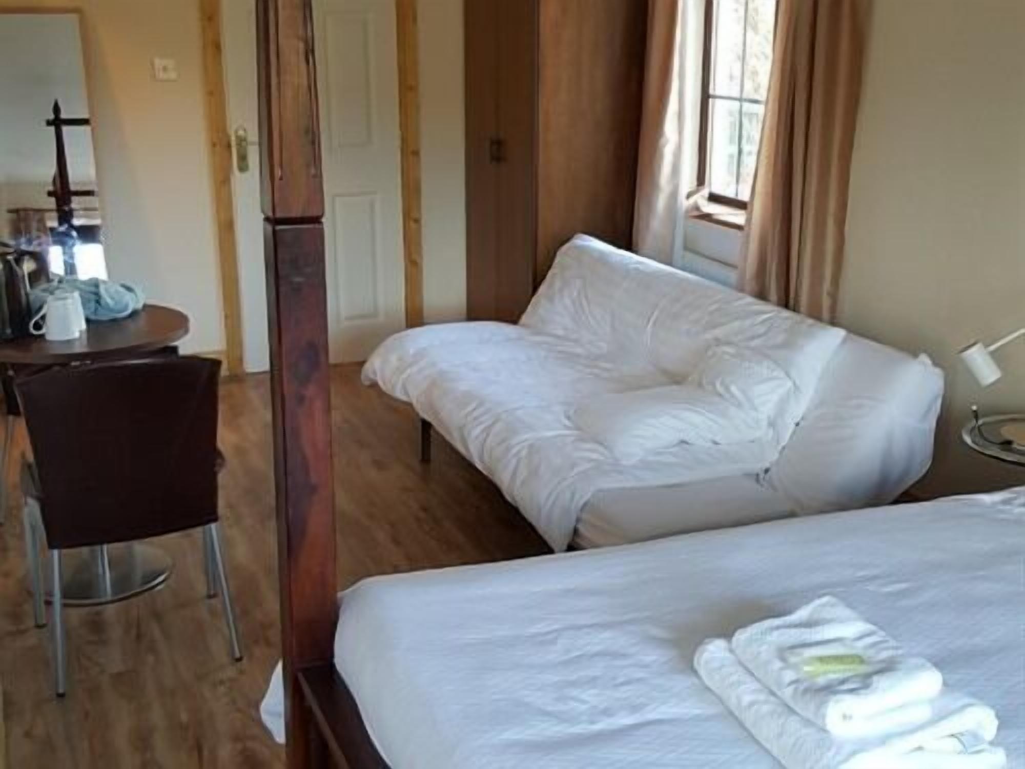 A hotel room with a bed, a chair, and a small table with a lamp.
