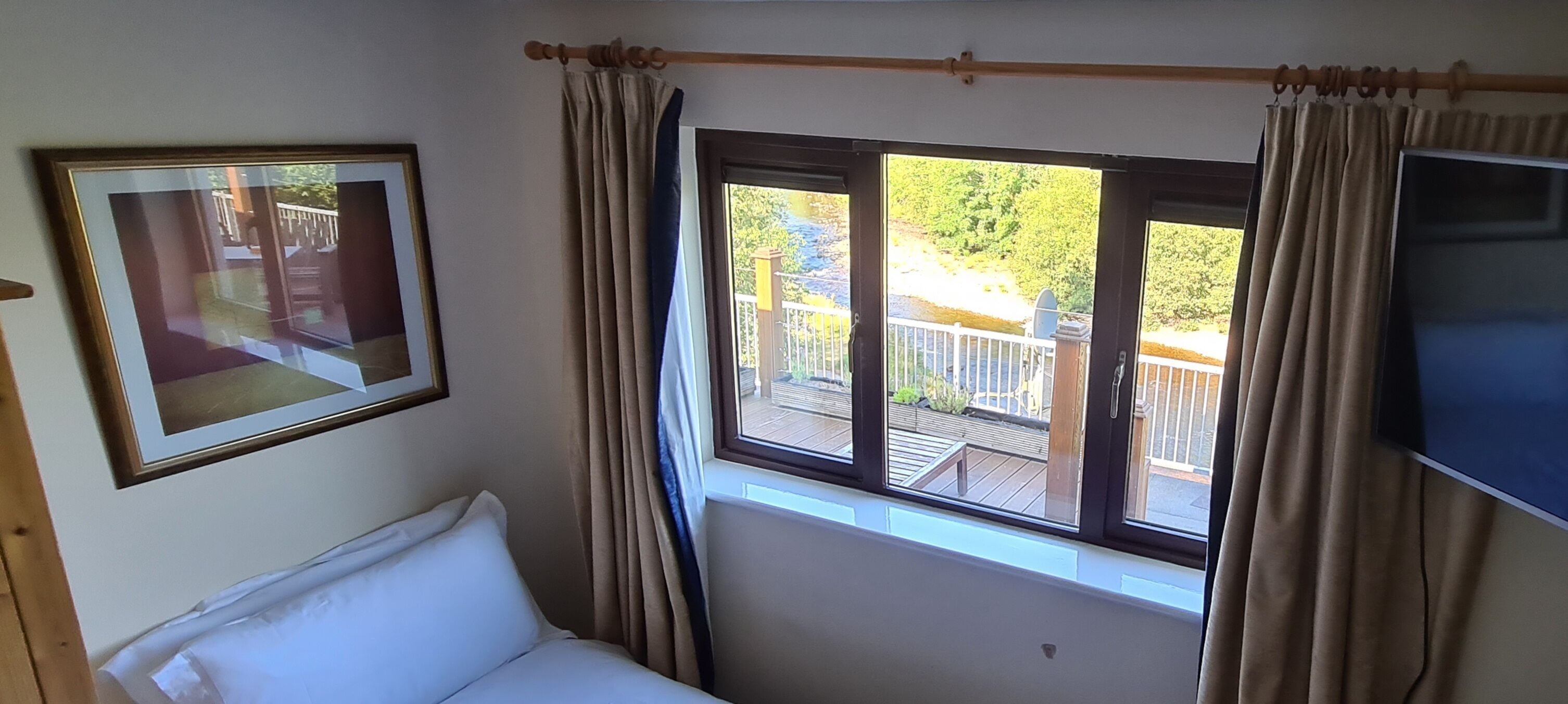 A bedroom with a bed, a window with curtains, a TV, and a framed picture on the wall.