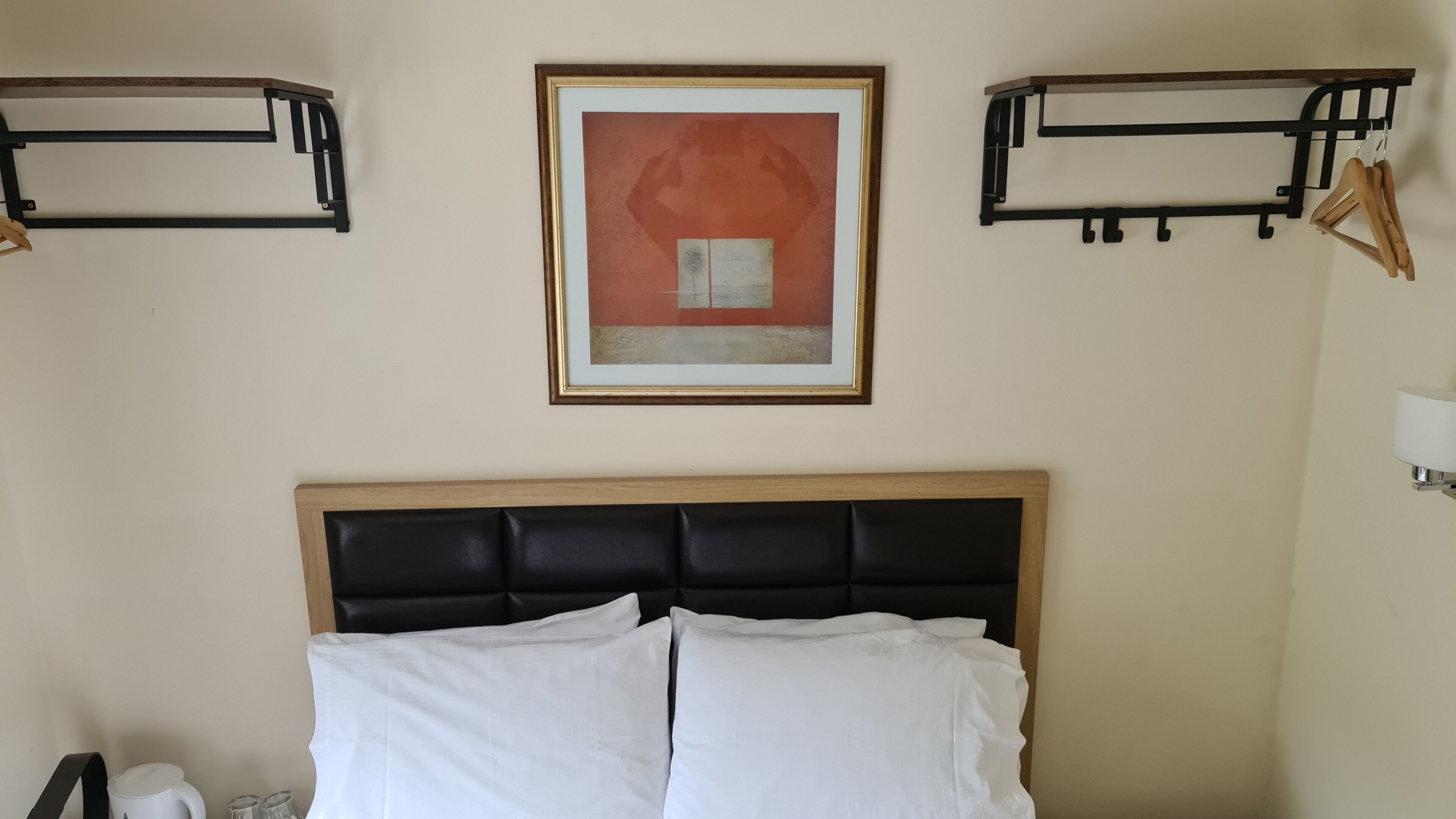 Ein Hotelzimmer mit einem Bett, einem gerahmten Kunstwerk, zwei schwarzen Wandraften und einer Lampe.