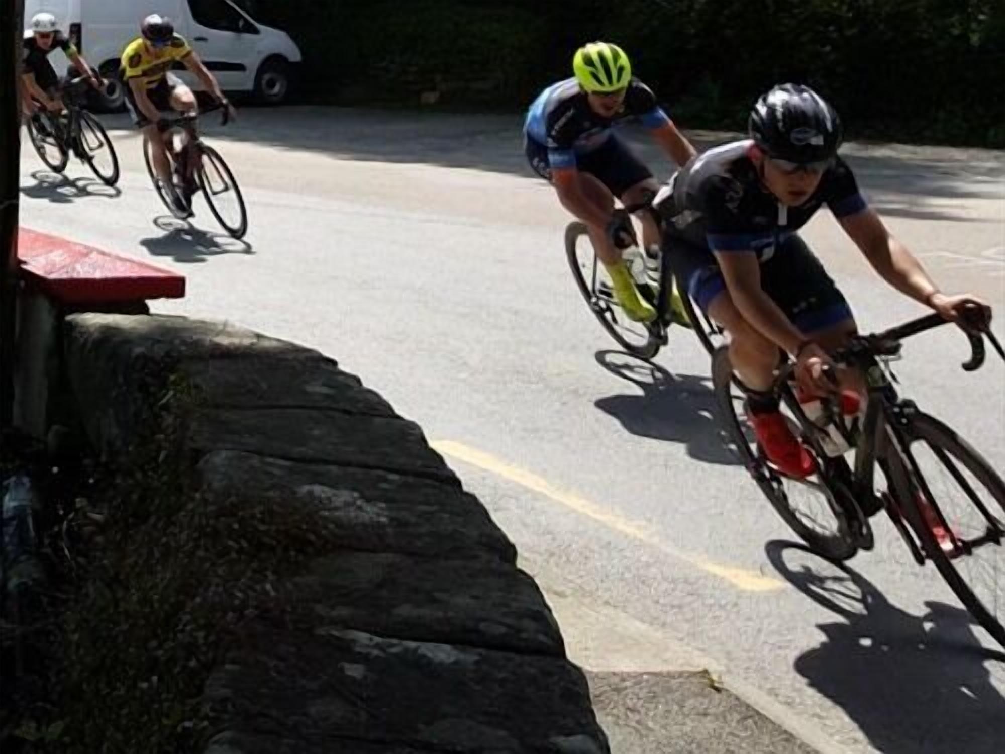 A group of cyclists on a paved road with a stone wall on one side.