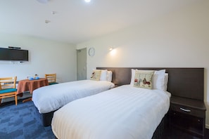 Habitación de hotel con dos camas, un televisor montado en la pared, una mesita con una silla y un reloj en la pared.