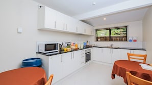 Une cuisine compacte avec des meubles blancs, un four à micro-ondes, un évier et une fenêtre donnant sur un espace verdoyant.