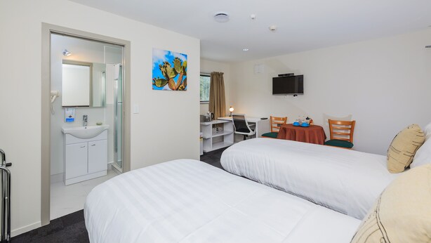 Une chambre d’hôtel avec deux lits, un bureau, une chaise, une télévision et une salle de bain équipée d’un lavabo et d’un miroir.
