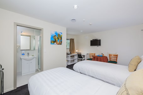 A hotel room with two beds, a desk, a chair, a TV, and a bathroom with a sink and mirror.