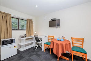 Habitación compacta con kitchenette, escritorio, dos sillas, mesa y televisor montado en la pared.