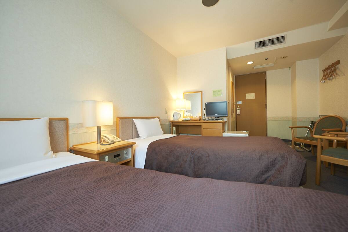 A hotel room with two beds, a desk with a computer, a chair, and a television.