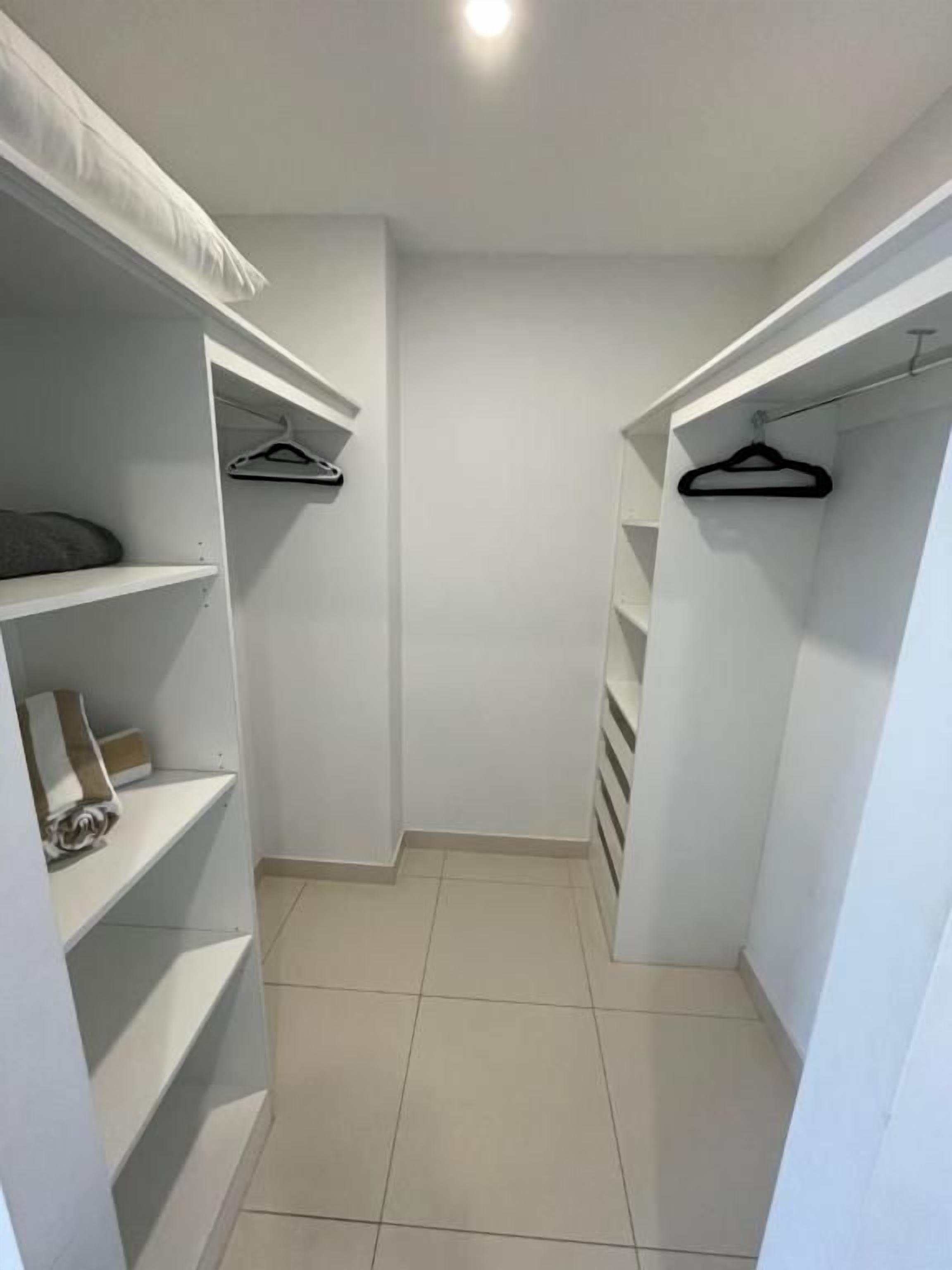 A narrow walk-through closet with white walls and tiled flooring.
