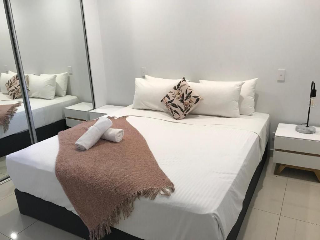 A neatly made bed with a white duvet, a brown throw blanket, and a floral pillow. There is a nightstand with a lamp and a power outlet on the wall.
