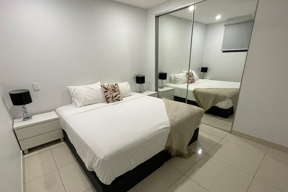 A modern bedroom with a large bed, bedside tables, a mirror, and a wardrobe.