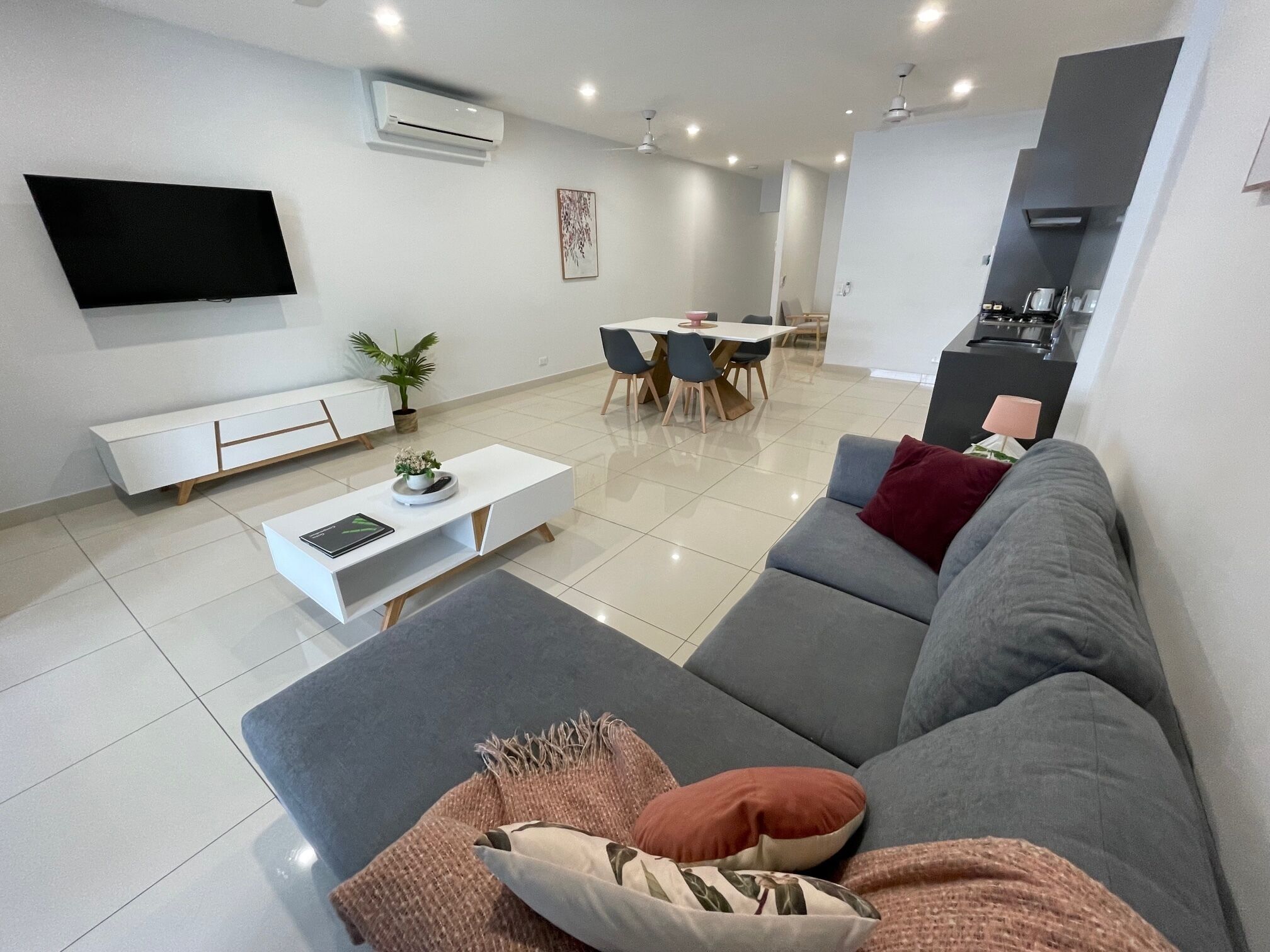 A modern living room with a grey sofa, a white coffee table, and a dining area with a table and chairs.