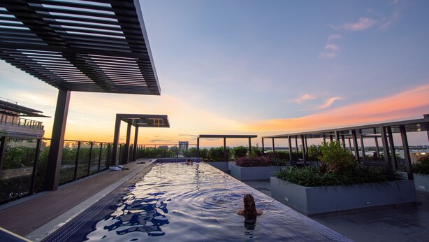 A rooftop infinity pool with a view of the sunset, surrounded by modern architecture and greenery. - Magnum Serviced Apartments (Darwin)