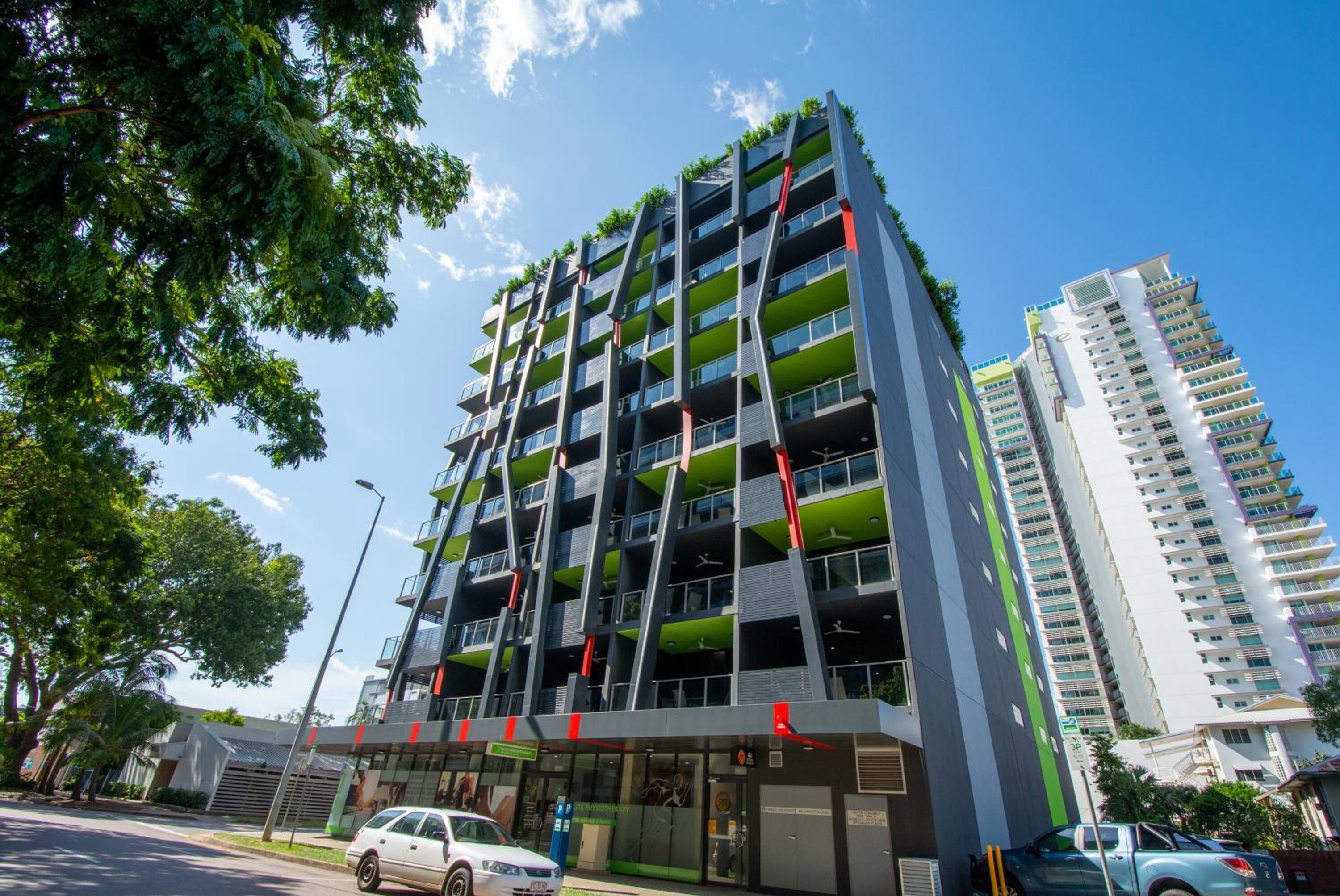 Un edificio de varios pisos con balcones, una tienda y un coche estacionado.