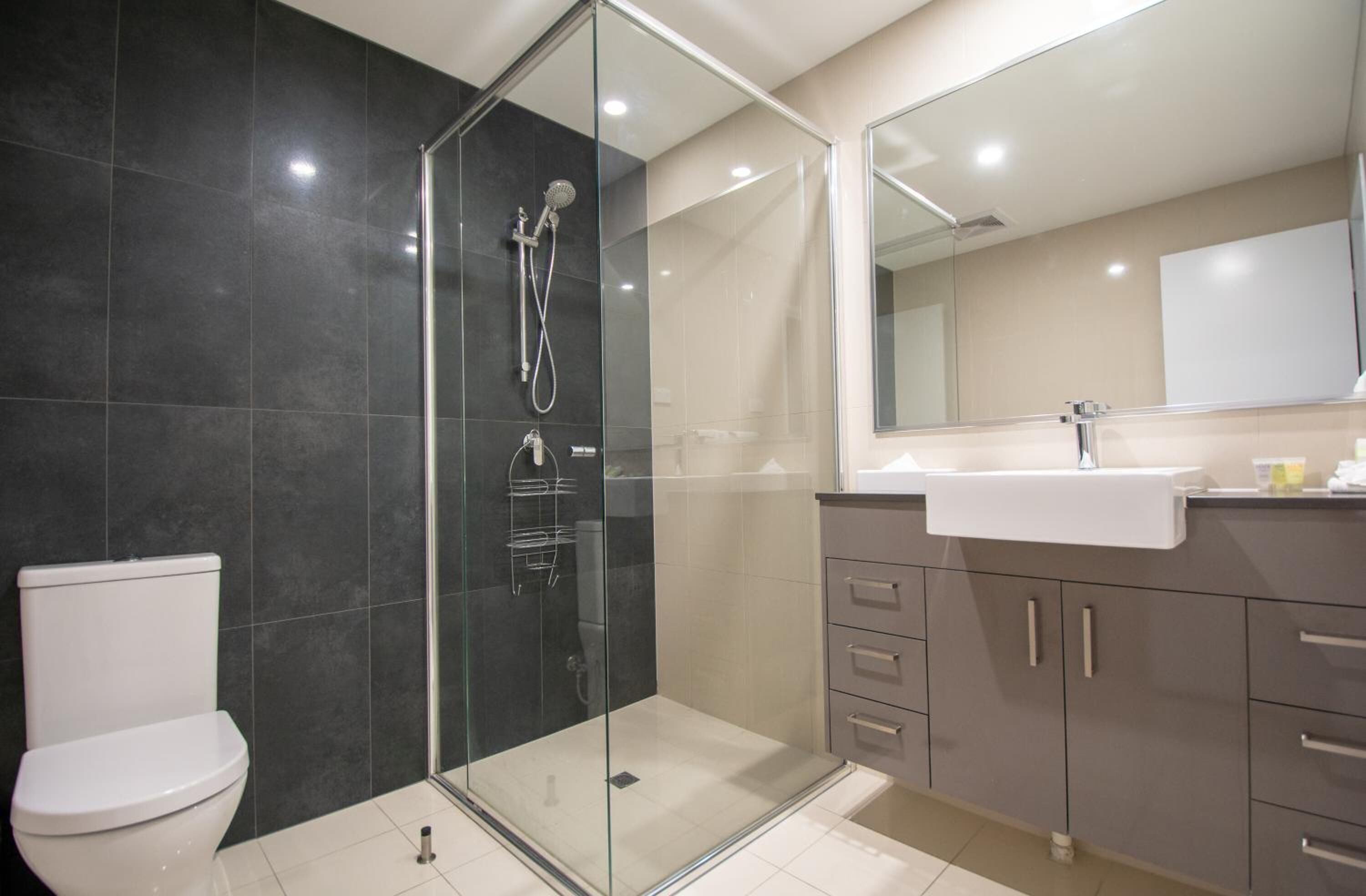 A modern bathroom with a glass-enclosed shower, a white toilet, and a vanity with a mirror.