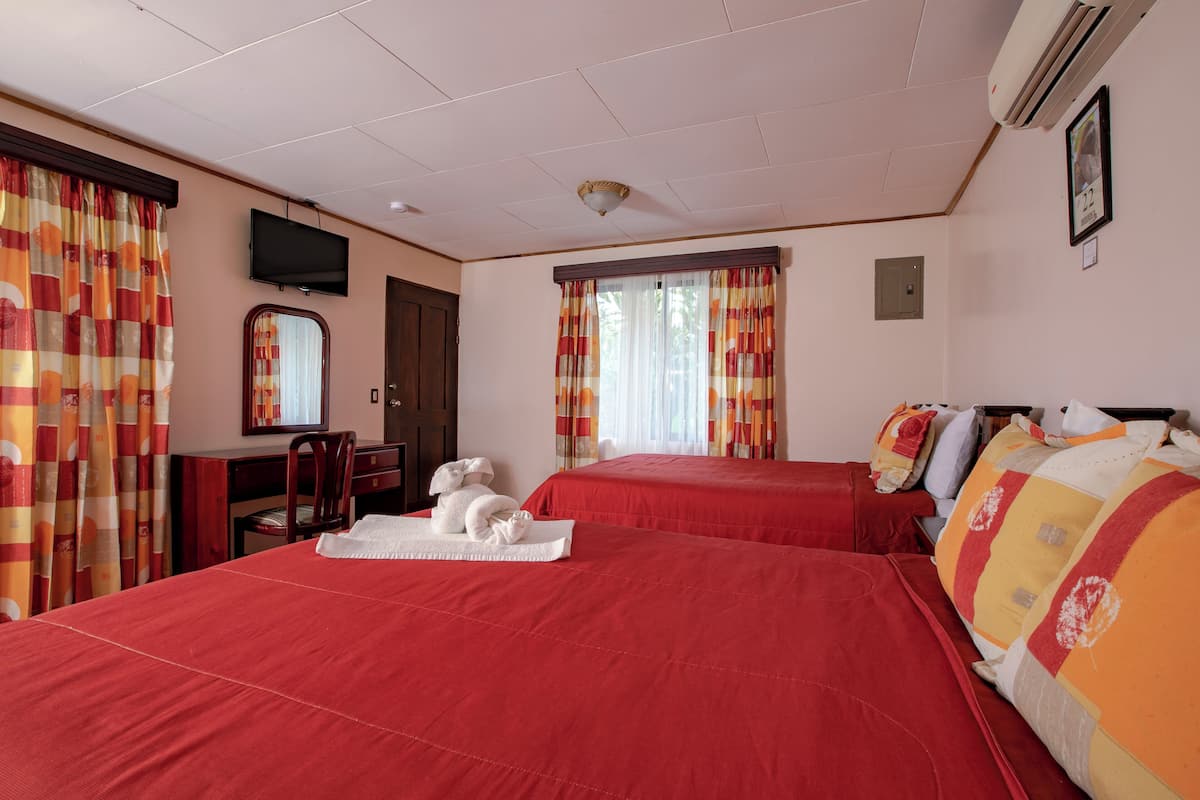 A hotel room with two beds, a desk, a chair, a television, and an air conditioning unit.