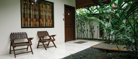 A patio with two wooden chairs, a door, and a window with a curtain.