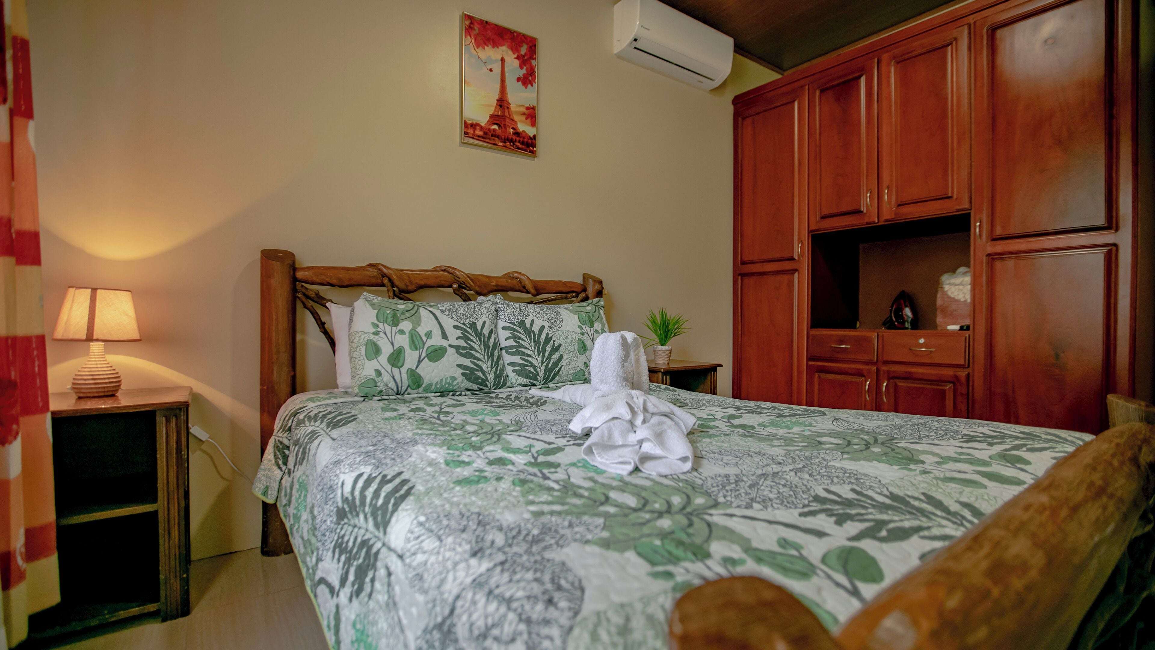 Un dormitorio con cama, mesita de noche, lámpara, planta en maceta y armarios de madera.