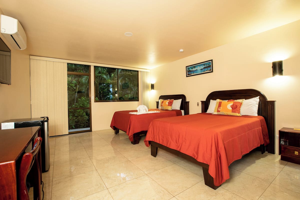 A hotel room with two beds, a desk, and a sliding glass door leading to a balcony.
