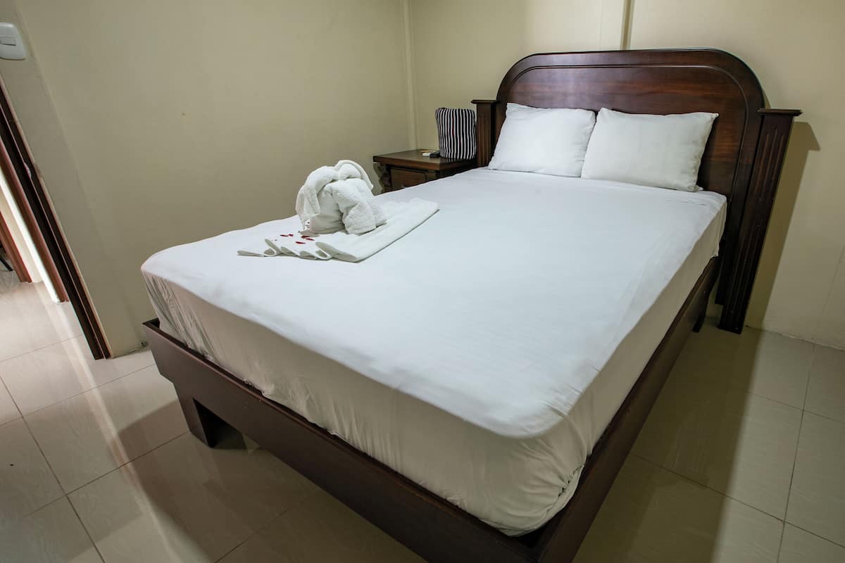 A neatly made bed with white linens, a wooden headboard, and a bedside table with a lamp and a striped pillow.