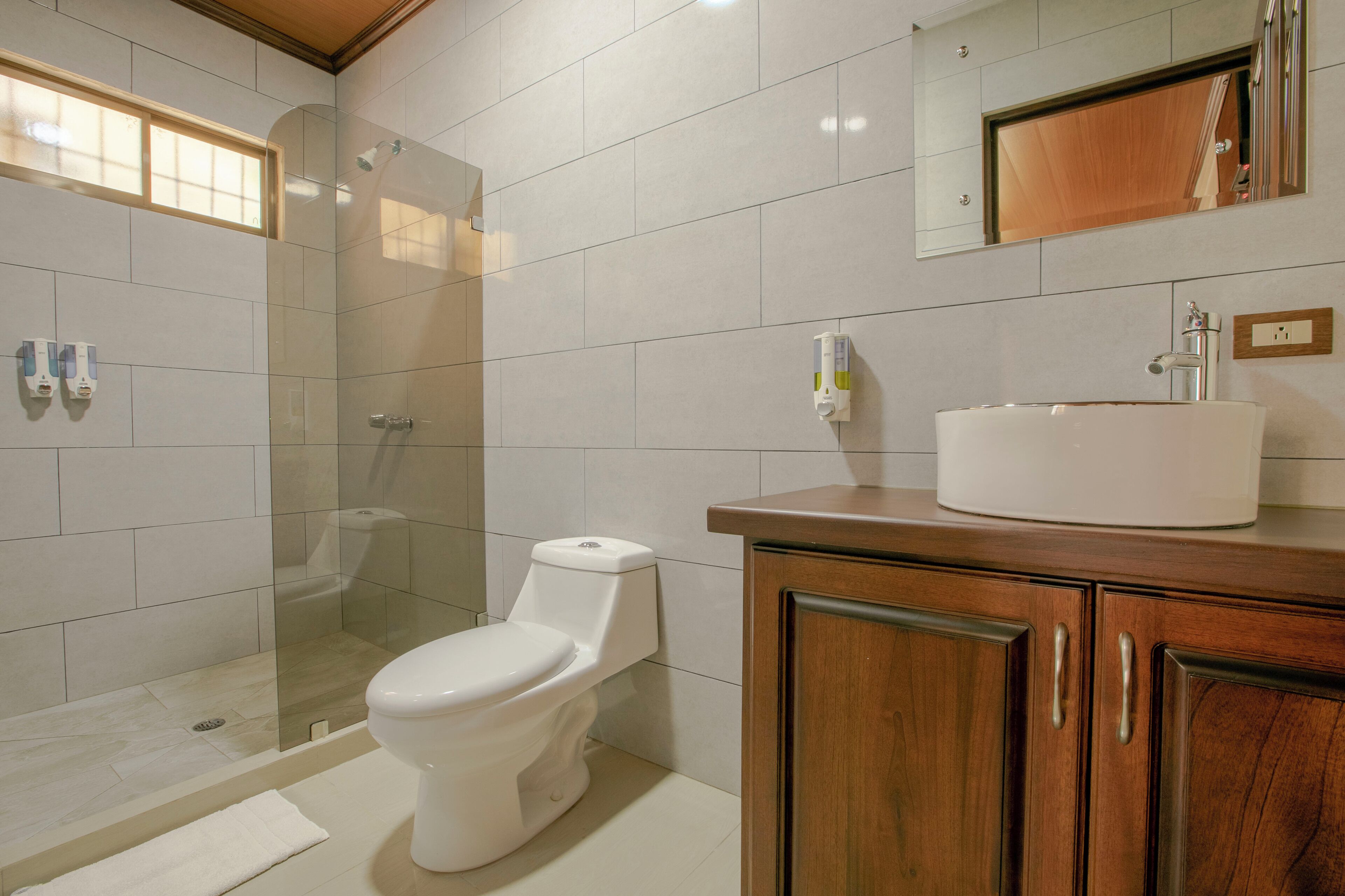 A modern bathroom with a glass shower enclosure, a toilet, and a vanity with a sink and mirror.