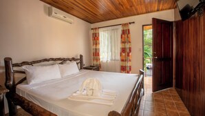 A neatly made bed with white linens and a towel, wooden headboard, and a wooden ceiling. - Hotel Las Orquideas (La Fortuna)