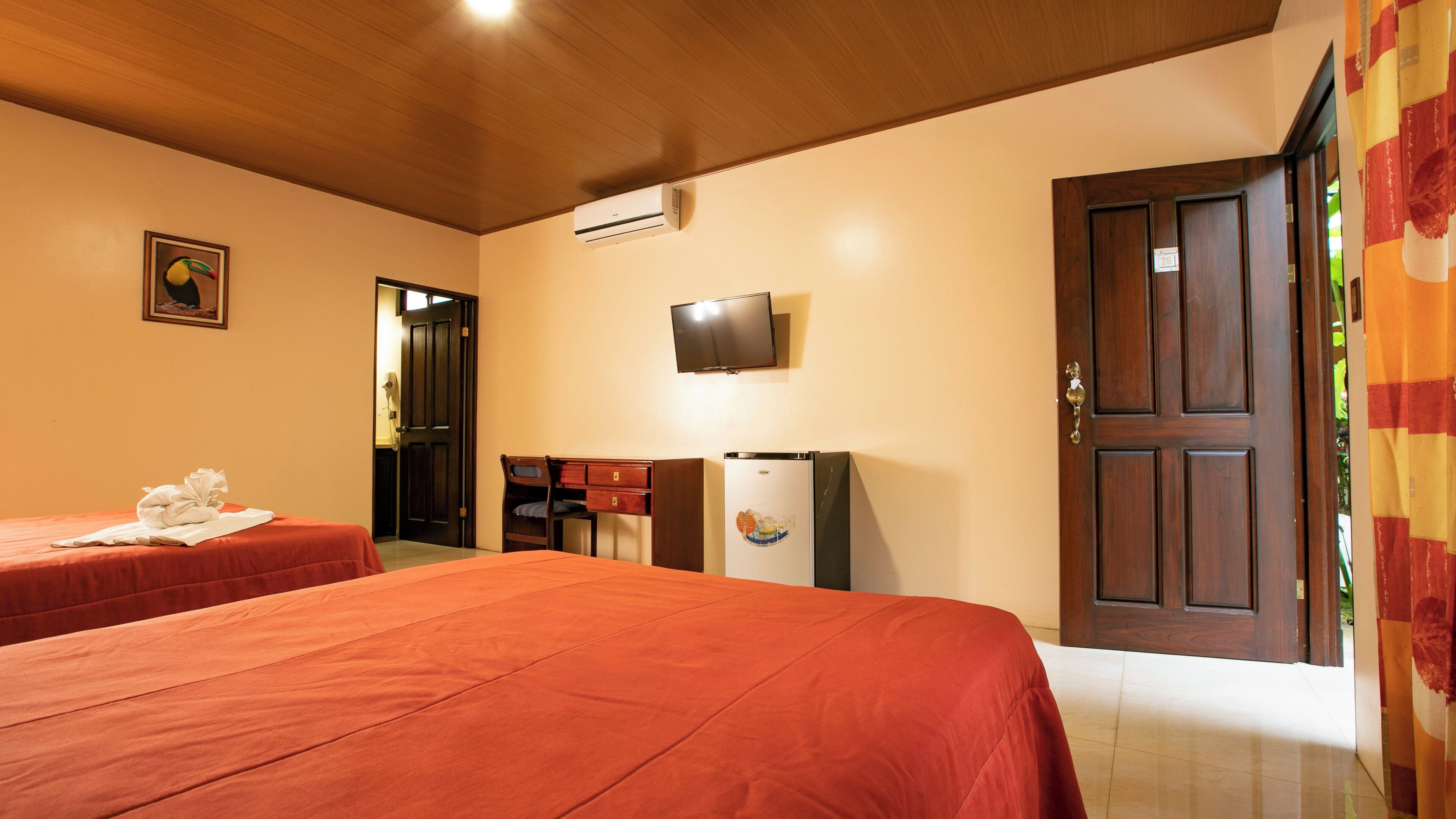 A hotel room with two beds, a television, an air conditioning unit, and a door with a number.