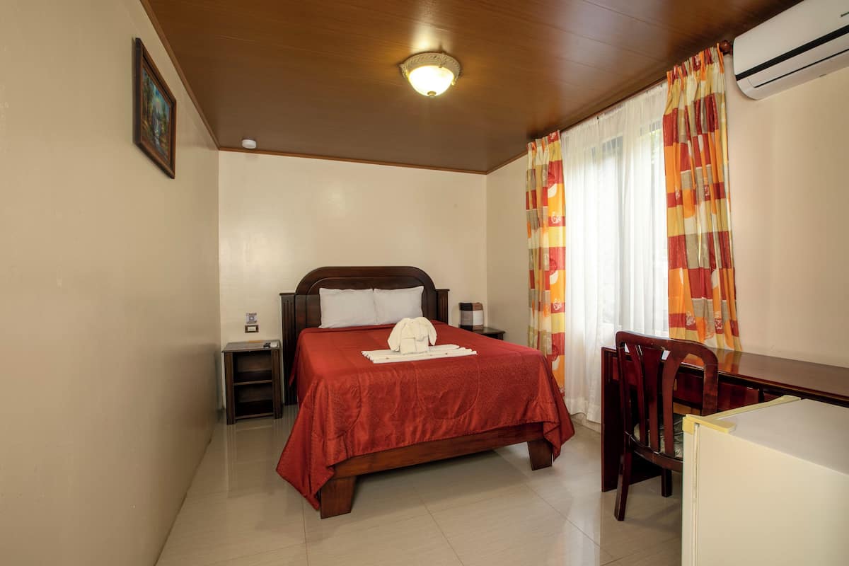 A bedroom with a wooden bed, a nightstand, a desk, and a chair.