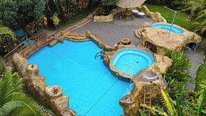 A large outdoor swimming pool with multiple sections, surrounded by natural rock formations and tropical plants. - Hotel Las Orquideas (La Fortuna)