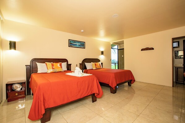 A hotel room with two beds, each with a red bedspread and pillows, a nightstand, a lamp, and a painting on the wall. - Hotel Las Orquideas (La Fortuna)