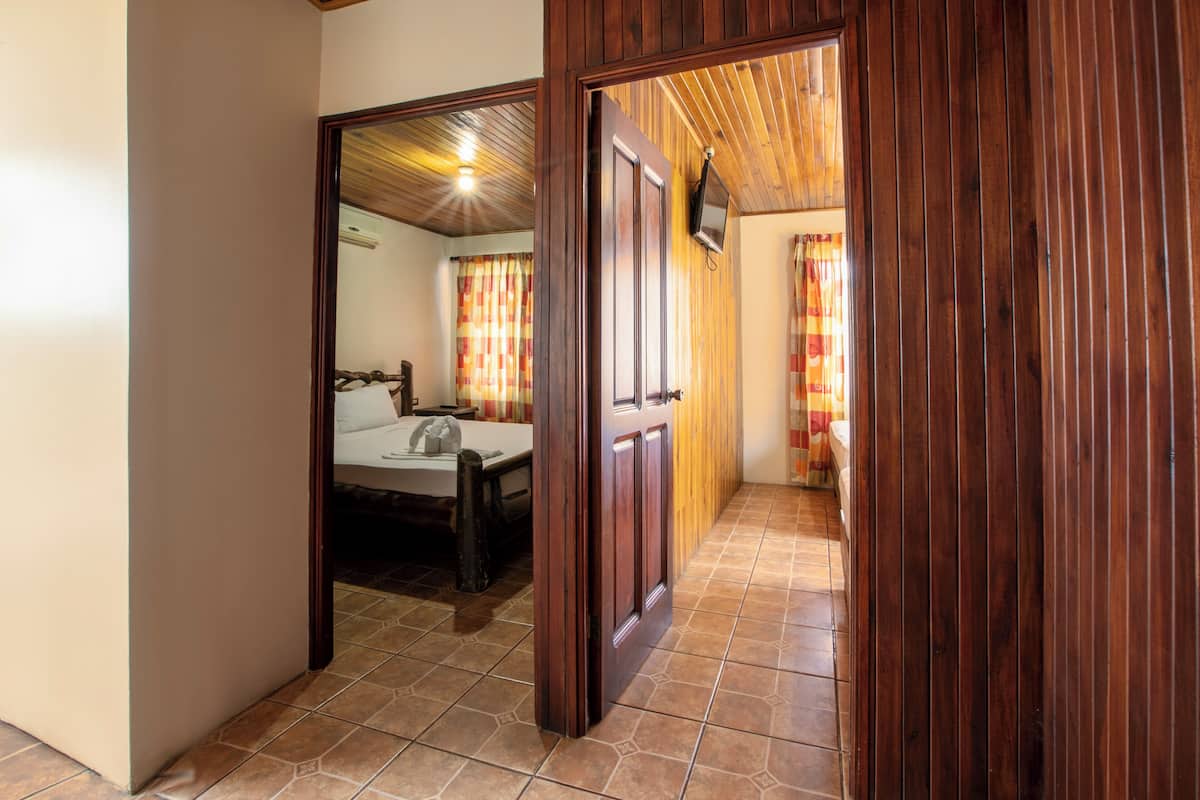 A hallway with wooden doors leading to a bedroom with a bed and a nightstand.