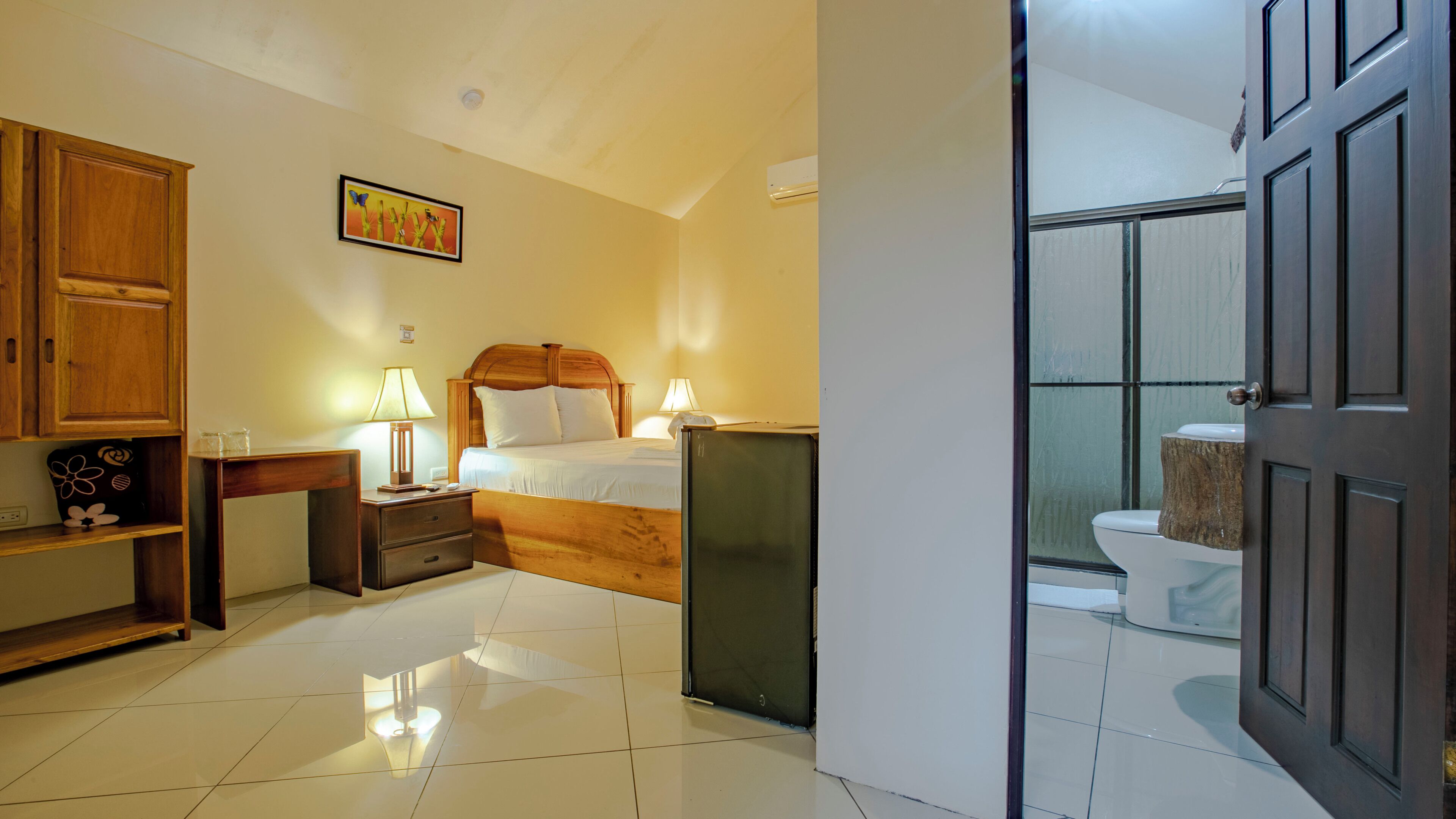 Ein Hotelzimmer mit Bett, Nachttischen, einer Lampe, einem Bild an der Wand und Blick ins Badezimmer durch eine offene Tür.