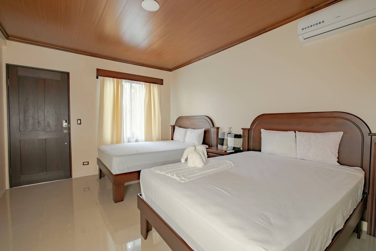 A hotel room with two beds, a wooden ceiling, and an air conditioning unit.