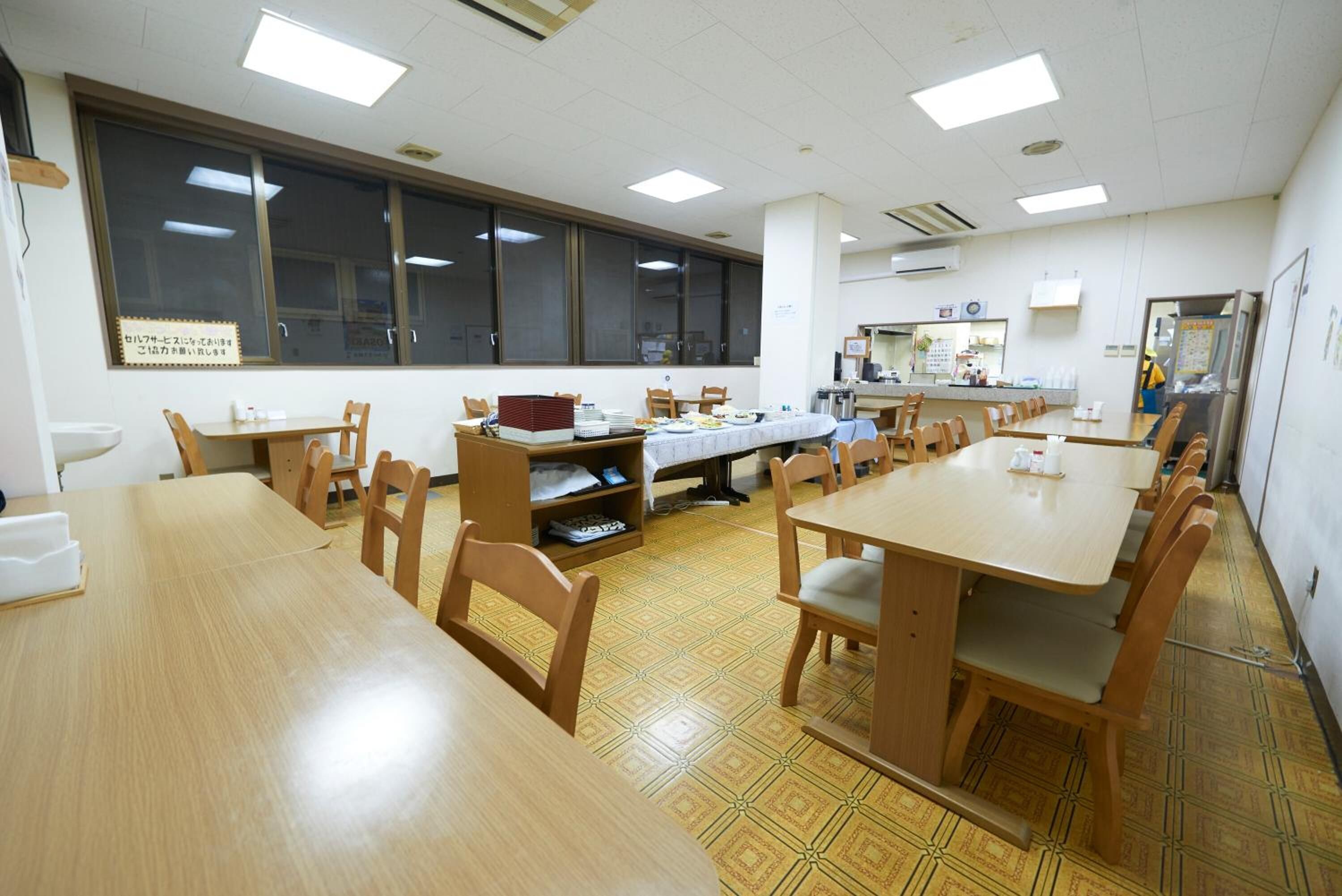 A dining area with wooden tables and chairs, a large window, and a tiled floor.