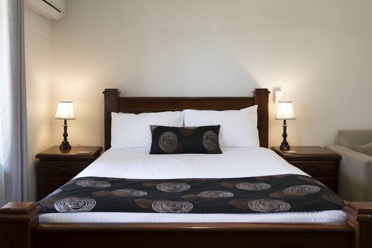 Een netjes opgemaakt bed met een beddengoed met een patroon, twee bedlampen en een houten hoofdbord.