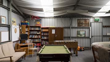 A room with a pool table, bookshelves, a sofa, and an exit sign.