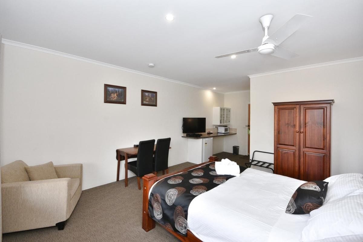 A hotel room with a bed, a desk with a chair, a television, a wardrobe, and a ceiling fan.
