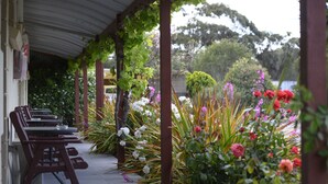 A covered outdoor seating area with tables and chairs, surrounded by lush greenery and flowering plants. - Inglewood Motel and Caravan Park (Inglewood)