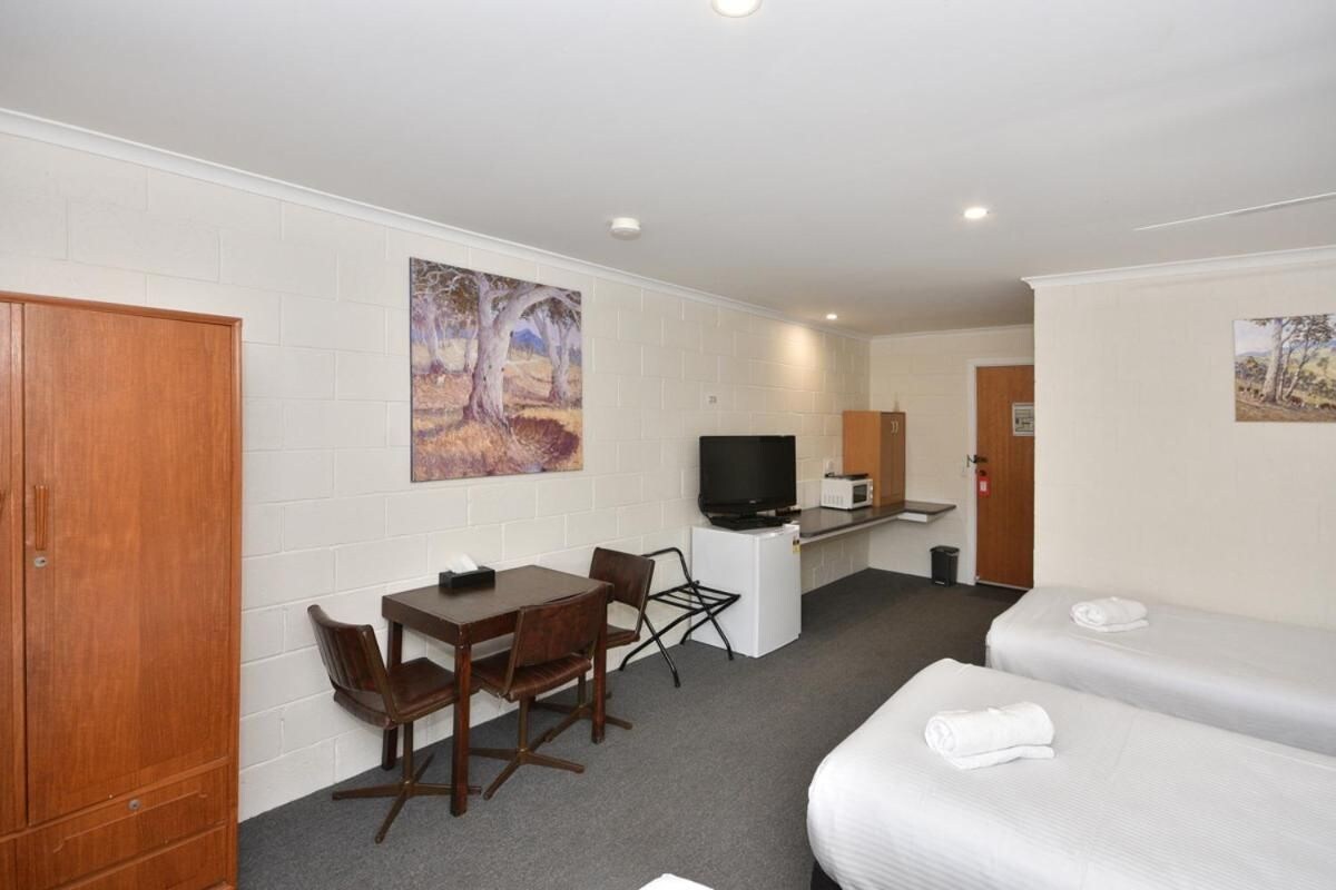 Een hotelkamer met een houten kast, een bureau met stoel, een televisie, een magnetron en twee bedden met handdoeken.