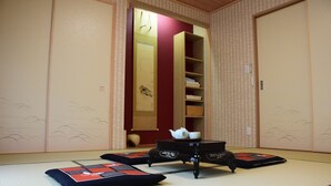 Une pièce avec un sol recouvert de tatamis, une petite table basse, des coussins et une étagère sur laquelle se trouvent une théière et des tasses.