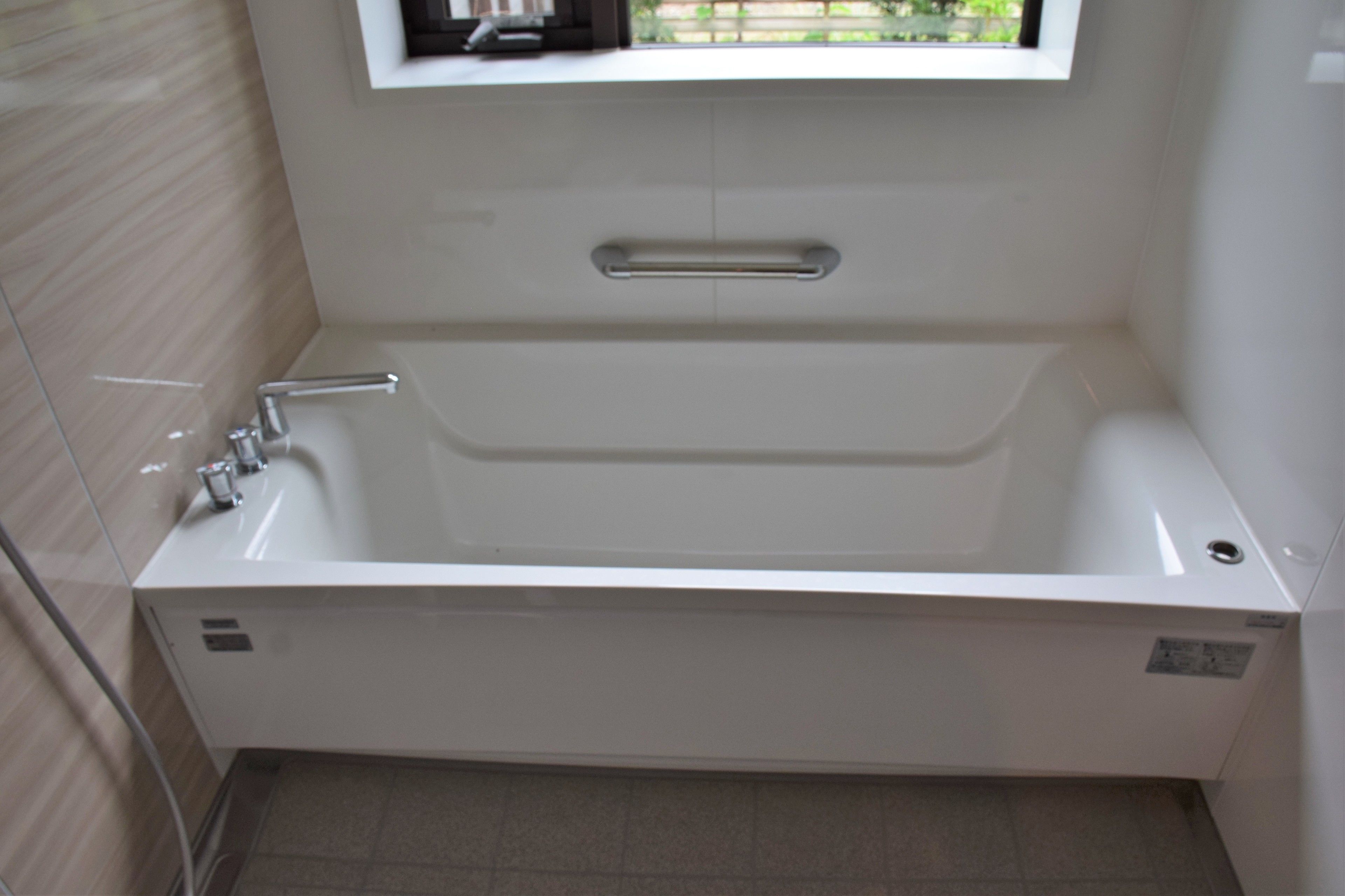 Un baño moderno con una bañera independiente, una ventana sobre el lavamanos y paredes con azulejos.