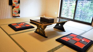 Une pièce avec un sol recouvert de tatamis, une petite table basse, des coussins et une fenêtre donnant sur un paysage verdoyant.