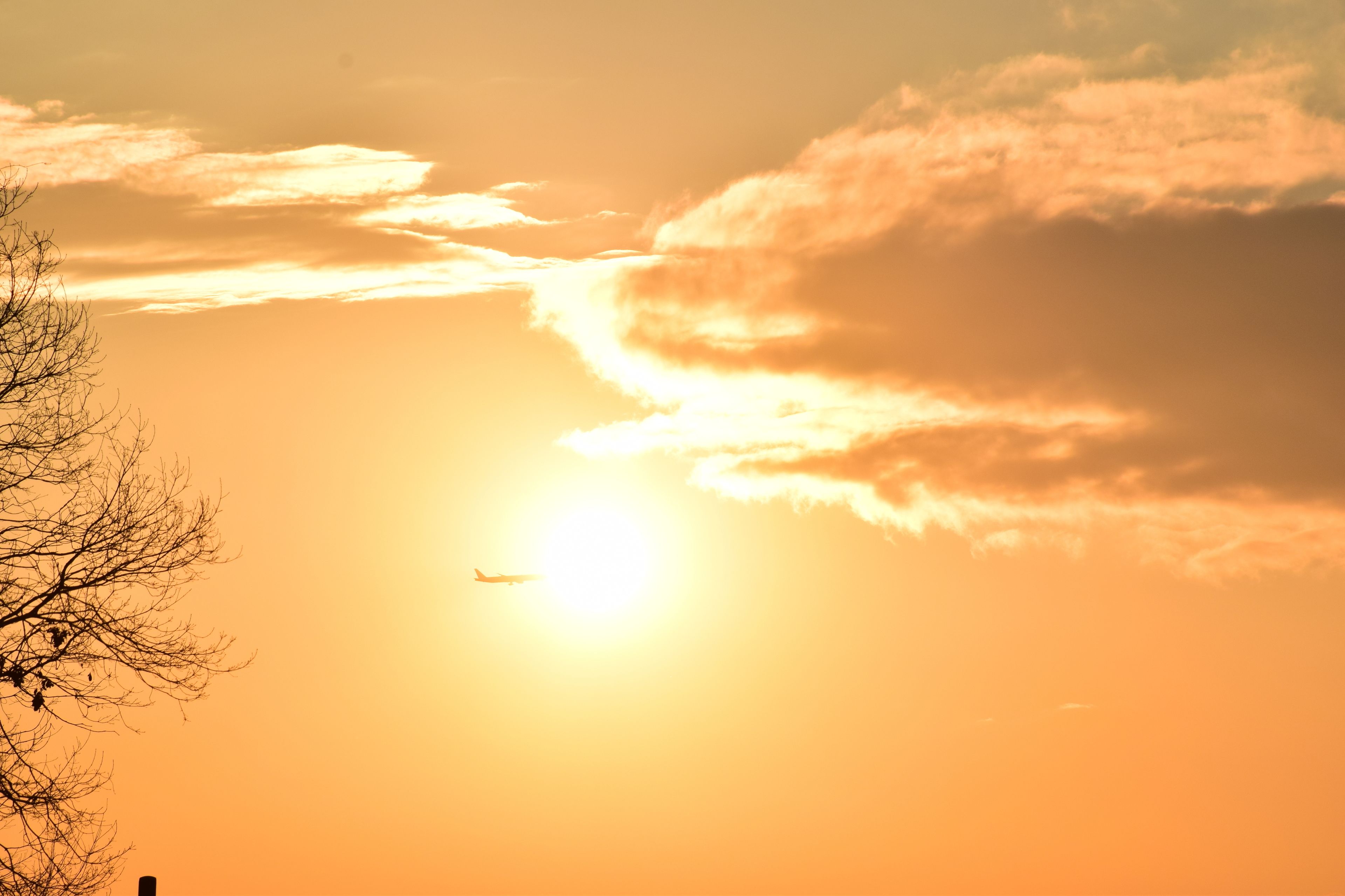 A sunset with a plane flying in the sky.