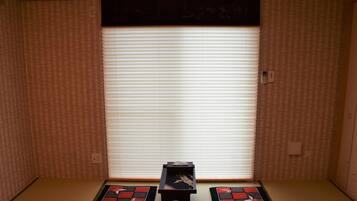 Una stanza con pavimento in tatami, un paravento scorrevole tipo shoji e un piccolo tavolo di legno con un oggetto decorativo.