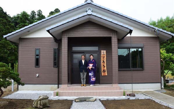 A traditional building with a modern entrance, a stone frog sculpture, and a wooden sign with Japanese characters.