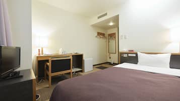 A hotel room with a bed, a desk with a computer, a television, and a small refrigerator.