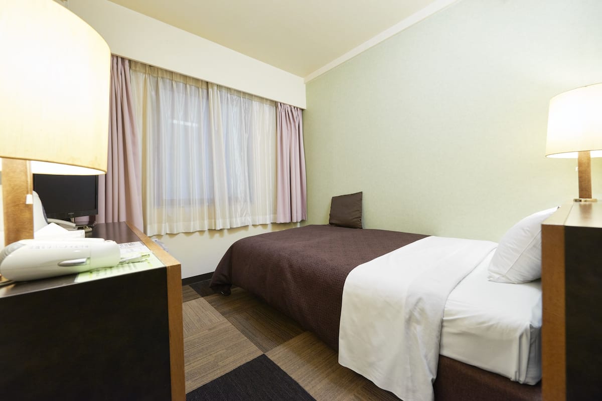 A hotel room with a bed, a desk with a computer, and a window with curtains.