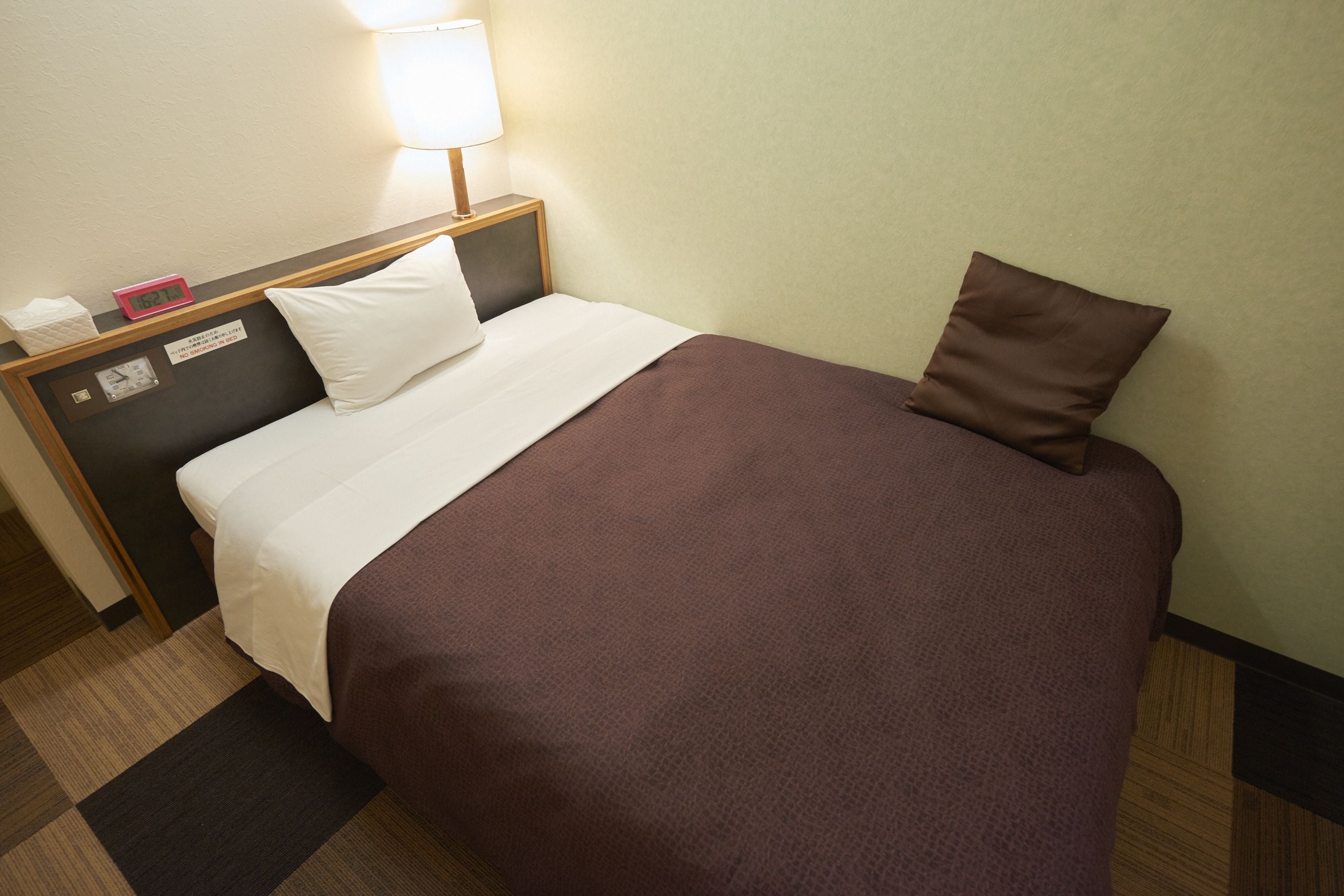 A neatly made bed with a white and brown bedspread, a pillow, and a nightstand with a lamp and a clock.