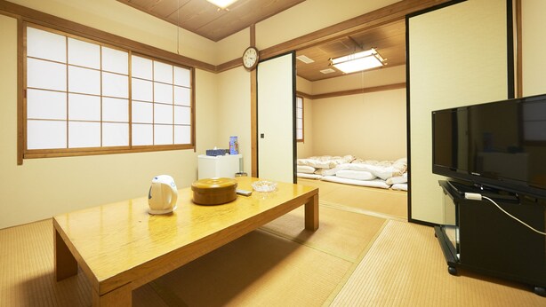 Una habitación japonesa tradicional con suelo de tatami, una mesa de madera, televisión y una puerta corredera que da a una zona de descanso.