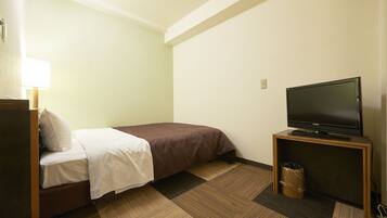 A hotel room with a bed, a television on a stand, and a trash bin.