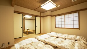 Un dormitorio de estilo japonés tradicional con suelo de tatami, una cama grande con ropa de cama blanca, una puerta corredera y un ventanal con diseño de cuadrícula.